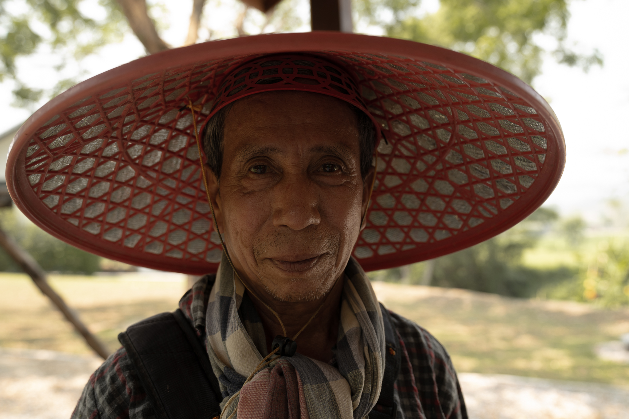 A farmer pauses beneath his woven sun hat, his face mapped by decades of seasons spent under an unforgiving sky.
