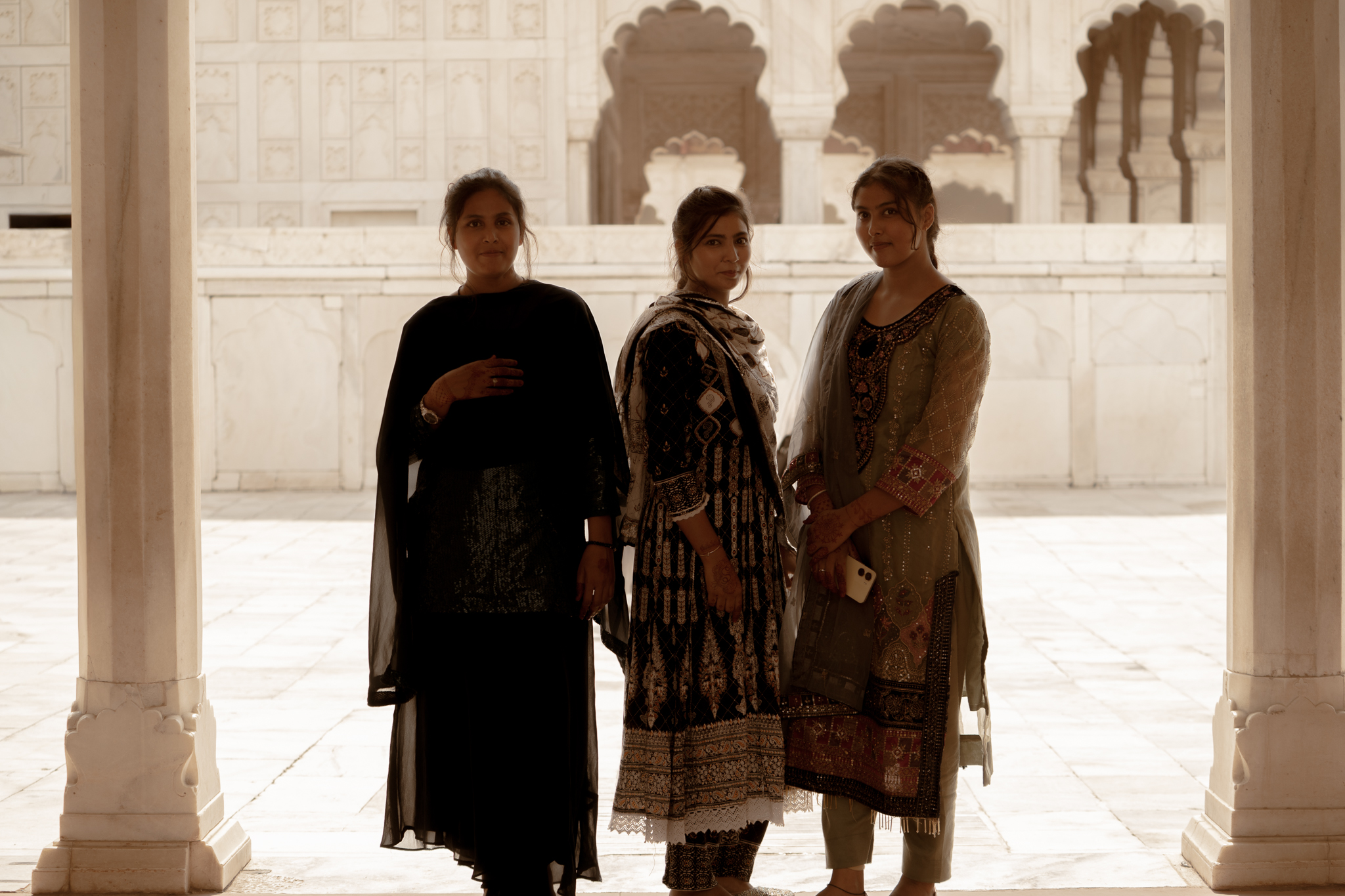 Visitors pause among the cool marble arches of a Mughal pavilion, framed against the glare of the courtyard beyond.